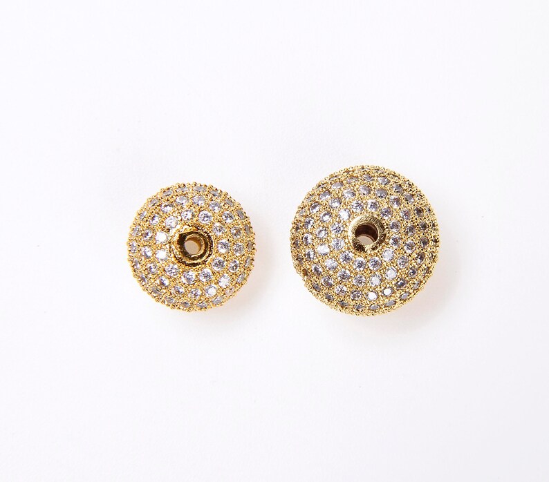 May include: Two gold-toned round beads with a hole in the center. The beads are covered in small, clear rhinestones.