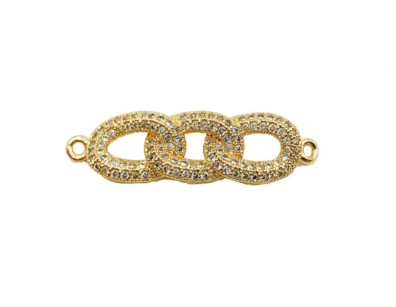 May include: Gold-toned jewelry connector featuring three interlocking oval links, each encrusted with small, clear crystals. The connector has small loops on each end for attachment, set against a white background.