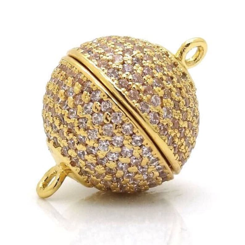 May include: Gold-toned magnetic clasp with a round, faceted design. The clasp is covered in small, clear rhinestones.