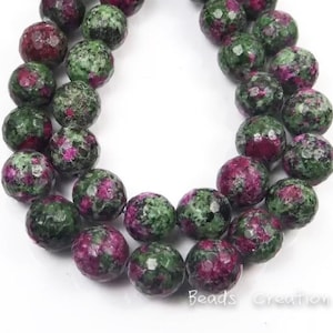 May include: A strand of green and pink gemstone beads. The beads are round and have a faceted finish. The beads are strung on a clear string.