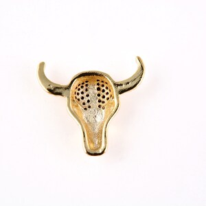 May include: Gold-toned bull head pendant with a detailed design. The pendant is hollow and has a textured surface.