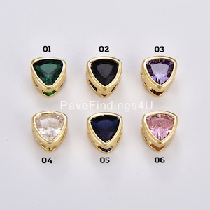 May include: Six gold-tone triangle-shaped jewelry findings with different colored stones: green, black, purple, clear, blue, and pink. The findings are labeled 01 through 06.