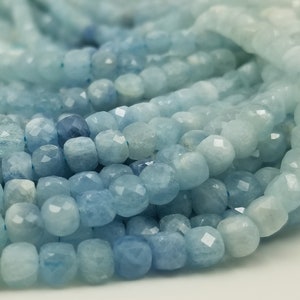 May include: Close-up of aquamarine gemstone beads. The beads are a light blue color with faceted surfaces, creating a sparkling effect. The beads are strung together, suggesting they are for jewelry making or crafting.