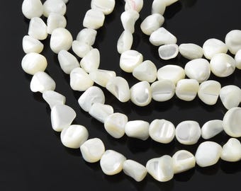 Puede incluir: Primer plano de varios hilos de cuentas blancas de forma irregular. Las cuentas tienen un brillo nacarado y están ensartadas, creando un efecto de capas. El fondo es negro liso, lo que proporciona contraste con las cuentas brillantes.