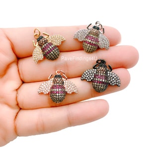 May include: Four bee-shaped pendants with intricate detailing. Each bee features a body of small, colorful gemstones, with wings and accents in gold, silver, and rose gold tones. The pendants are designed for jewelry making.