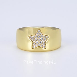Op de afbeelding: Een gouden ring met een stervormig ontwerp. De ster is bezet met kleine, heldere zirkonia-stenen.