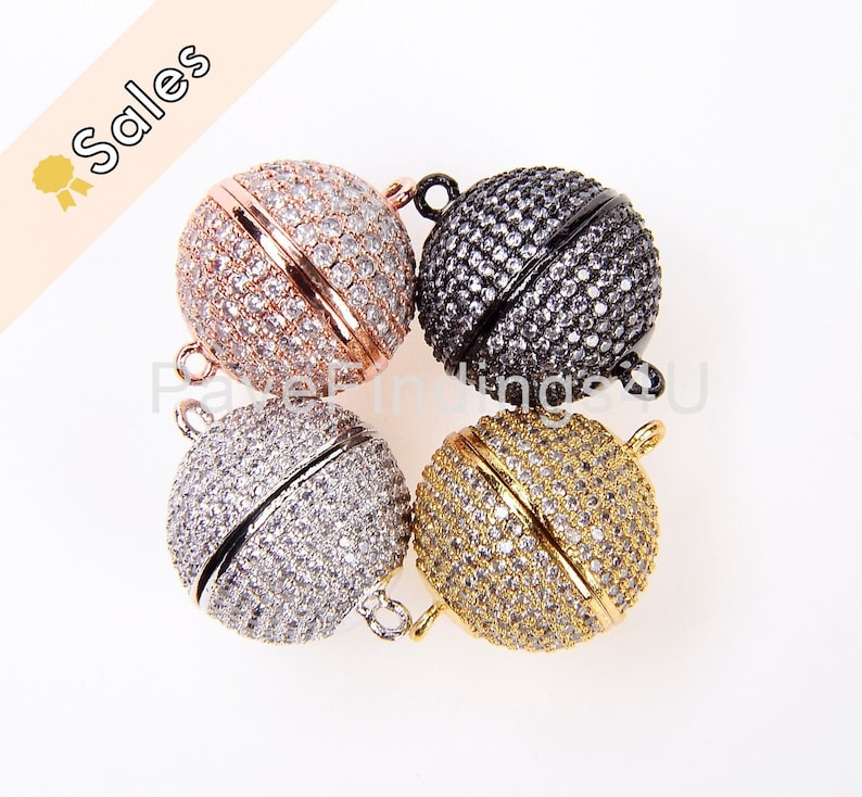 May include: Four round magnetic clasps for jewelry making. The clasps are made of metal and have a pave setting of clear rhinestones. The clasps are shown in four different colors: rose gold, silver, black, and gold.