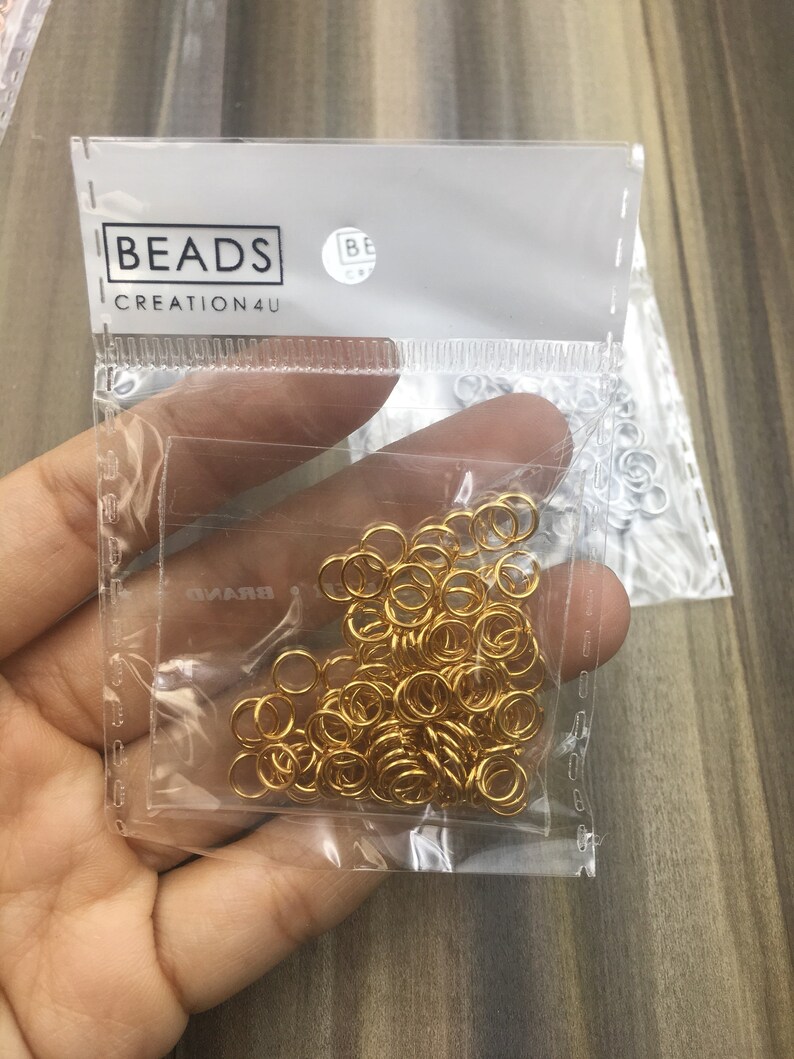 May include: A clear plastic bag filled with gold jump rings. The bag has a white label with the text "BEADS CREATION4U" printed on it.