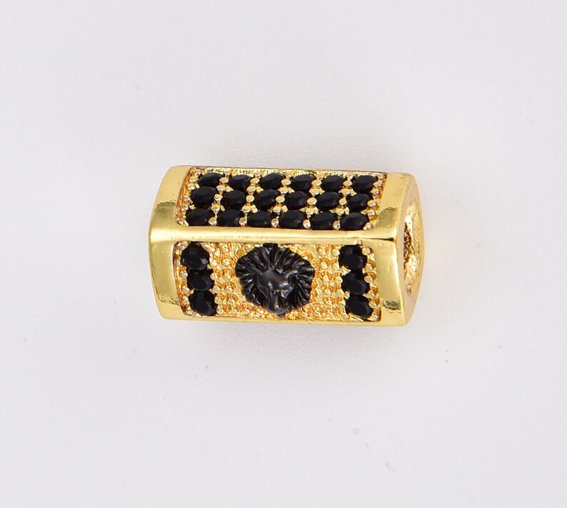 May include: Gold-toned bead with a black lion head design and black cubic zirconia stones.