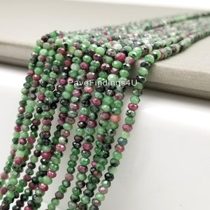 May include: A strand of green and pink faceted gemstone beads. The beads are small and round, and they are strung on a clear thread. The beads are arranged in a loose, flowing pattern.