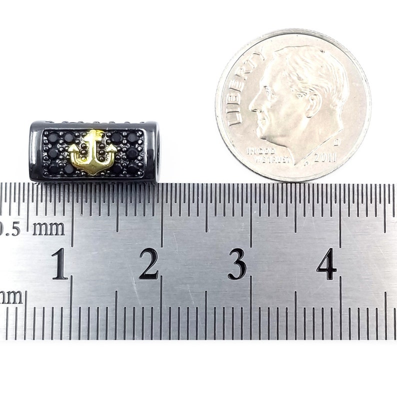 May include: Black and gold anchor charm with black cubic zirconia stones. The charm is about 1 inch long and is measured against a ruler.