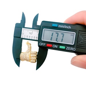 May include: A gold thumbs up charm with clear rhinestones, measured at 17.7 mm with a digital caliper.