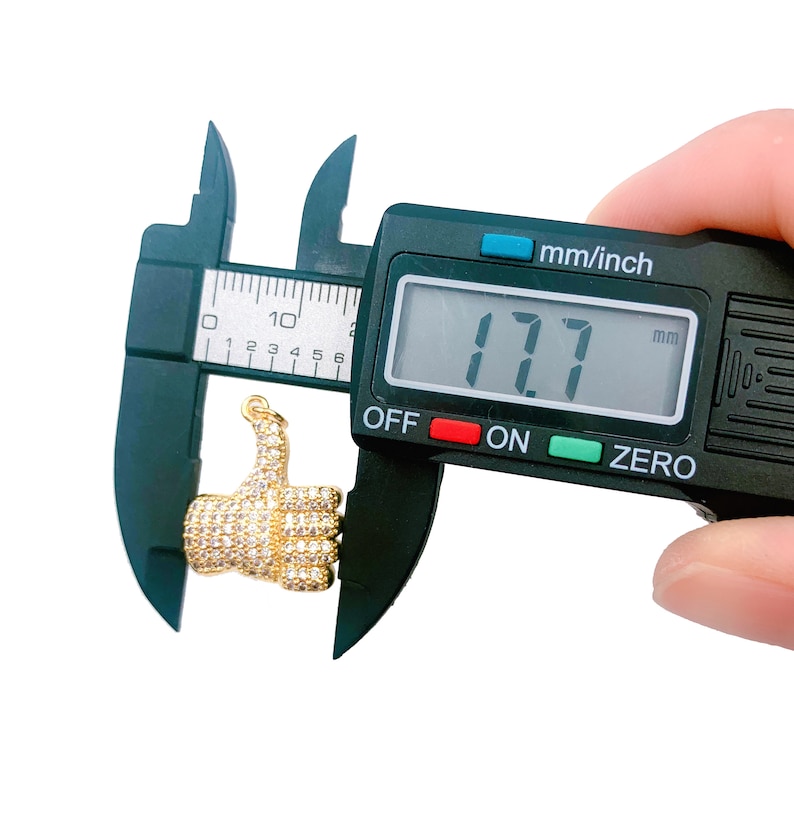 May include: A gold thumbs up charm with clear rhinestones, measured at 17.7 mm with a digital caliper.