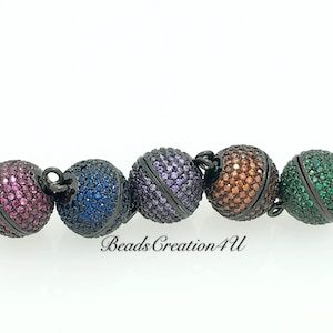 May include: Five magnetic clasps for jewelry making. The clasps are round and have a black metal finish. Each clasp is covered in colorful rhinestones. The colors are pink, blue, purple, orange, and green.