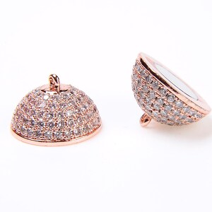 May include: Two rose gold tone metal dome shaped bead caps with clear cubic zirconia stones. The bead caps are designed to be used as end caps for necklaces or bracelets.