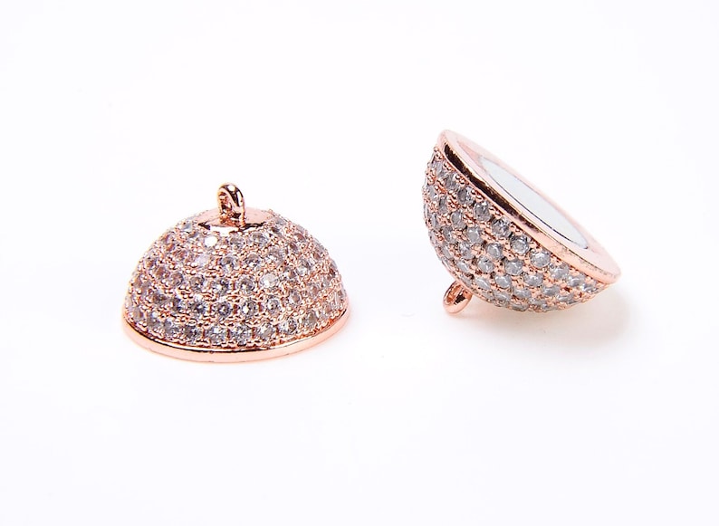 May include: Two rose gold tone metal dome shaped bead caps with clear cubic zirconia stones. The bead caps are designed to be used as end caps for necklaces or bracelets.