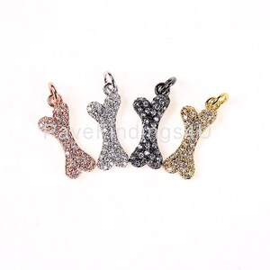 May include: Four bone-shaped charms with clear crystal accents. The charms are in rose gold, silver, black, and gold.