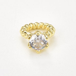May include: A gold ring featuring a large, clear, round gemstone. The ring band has a twisted rope design. The gemstone is held by six prongs. The ring is set against a white background.