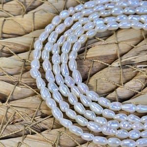 May include: A strand of white oval-shaped freshwater pearls. The pearls are strung on a clear thread and are arranged in a loose, flowing pattern.