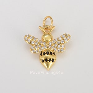 May include: Gold bee charm with clear and black cubic zirconia stones. The bee has a detailed design with wings, a body, and a stinger.