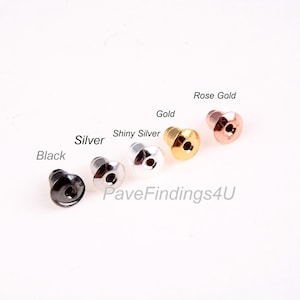May include: Six earring backs in different colors: black, silver, shiny silver, gold, and rose gold. The earring backs are made of metal and have a small hole in the center.