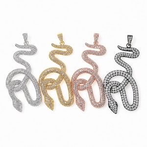 Pode incluir: Quatro pingentes em forma de cobra dispostos em fila, cada um coberto com pequenas pedras transparentes. Os pingentes têm acabamentos em tons metálicos prateado, dourado, ouro rosa e preto, e cada um possui uma pequena argola para corrente.