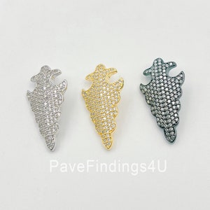 May include: Three pendant charms in the shape of a stylized flame, each with a different metal finish: silver, gold, and black. Each charm is covered in clear cubic zirconia stones.