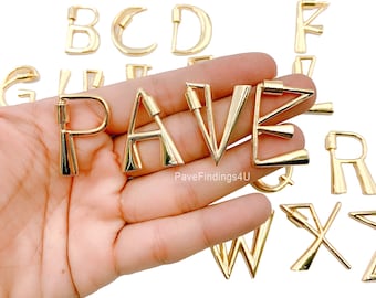 Può includere: Ciondoli in metallo dorato a forma di lettere dell'alfabeto, tra cui le lettere P, A, V, E, B, C, D, F, G, R, W, X e Z. Le lettere sono in stile moderno e geometrico.