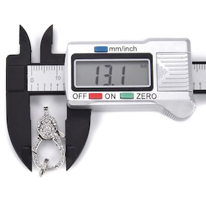 May include: A silver-toned clasp with clear cubic zirconia stones, measured at 13.1 mm using a digital caliper.