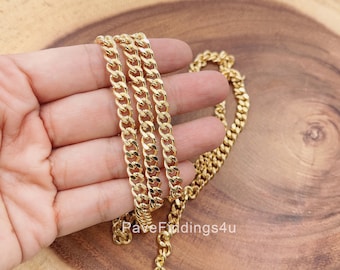 May include: A gold-colored curb chain necklace displayed on a wooden surface. The chain is made of interlocking links, creating a textured appearance. The necklace is held in a hand, showcasing its length and design. The chain is a jewelry item.