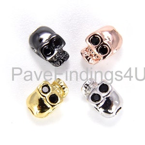 Puede incluir: Cuatro cuentas con forma de calavera en diferentes acabados metálicos: negro, oro rosa, oro y plata. Cada cuenta tiene detalles de ojos negros.