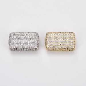 May include: Two rectangular jewelry beads, one silver-toned and one gold-toned, each featuring a dense pavé setting of small, clear, reflective stones covering the entire top surface and rounded edges of the rectangular metal base.