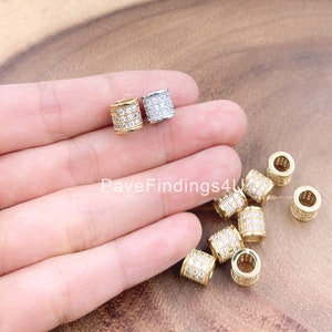 May include: A close-up of a hand holding a variety of gold and silver spacer beads. The beads are all round and have a pave setting of clear cubic zirconia stones. The beads are approximately 8mm in diameter.