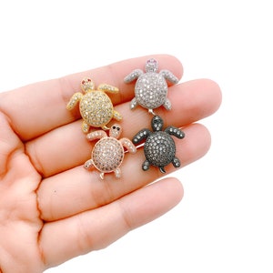 May include: Four turtle charms with a pave setting of clear rhinestones. The turtles are in gold, rose gold, silver, and black.