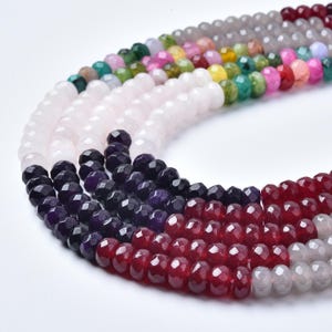 May include: Close-up of several strands of faceted gemstone beads in various colors. The beads include shades of pink, white, purple, red, green, yellow, and gray. The beads are strung together, creating a textured and colorful display.