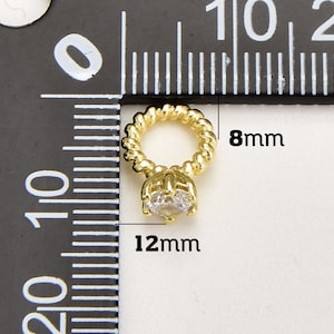 May include: A gold-coloured pendant featuring a clear, round gemstone. The pendant has a twisted rope-like loop, measuring 8mm in diameter, and the gemstone setting is 12mm wide. The jewellery is displayed against a ruler background.