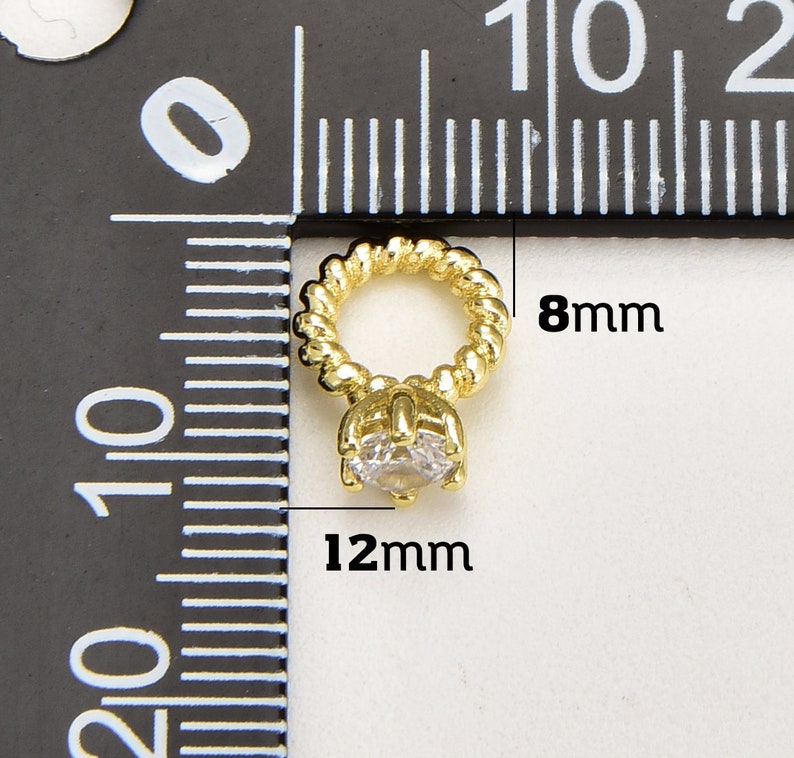 May include: A gold-coloured pendant featuring a clear, round gemstone. The pendant has a twisted rope-like loop, measuring 8mm in diameter, and the gemstone setting is 12mm wide. The jewellery is displayed against a ruler background.