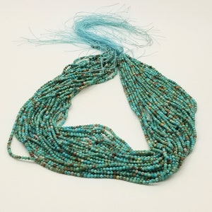 May include: A strand of turquoise beads, approximately 20 inches long, with a light blue tassel. The beads are a mix of light and dark turquoise colors, with some brown and black speckles.