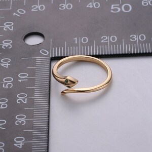 May include: A gold snake ring with green gemstone eyes. The ring is adjustable and can be worn on any finger.