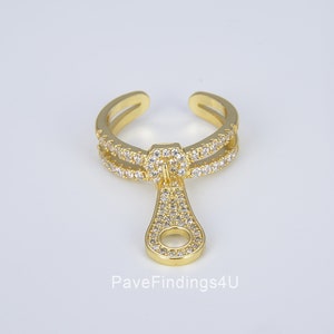 May include: Gold-tone adjustable ring with a double band of pave-set clear cubic zirconia stones. A dangling charm in the shape of a zipper pull is also pave-set with clear cubic zirconia stones.