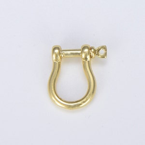 Pode incluir: Um grilhão de metal dourado com forma arredondada. O grilhão tem um pequeno laço de um lado.