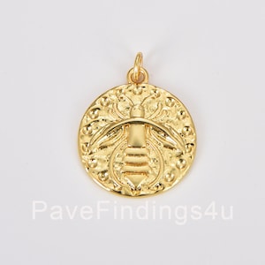May include: Gold-toned pendant featuring a detailed bee design. The bee is surrounded by a circle of small dots. The pendant is perfect for adding a touch of nature to any jewelry project.