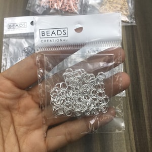 May include: A clear plastic bag filled with silver jump rings. The bag has a white label with the text "BEADS CREATION4U".