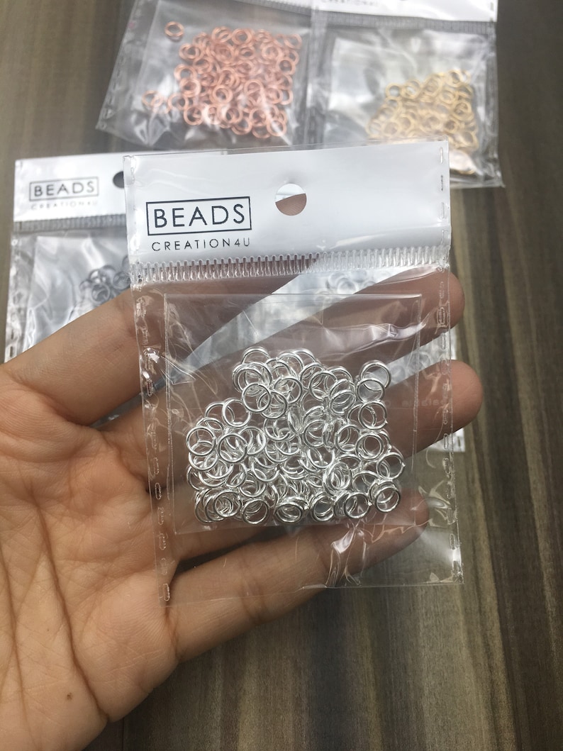 May include: A clear plastic bag filled with silver jump rings. The bag has a white label with the text "BEADS CREATION4U".