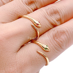 May include: Two gold snake rings with red and green gemstones. The rings are worn on the index and middle fingers of a hand.