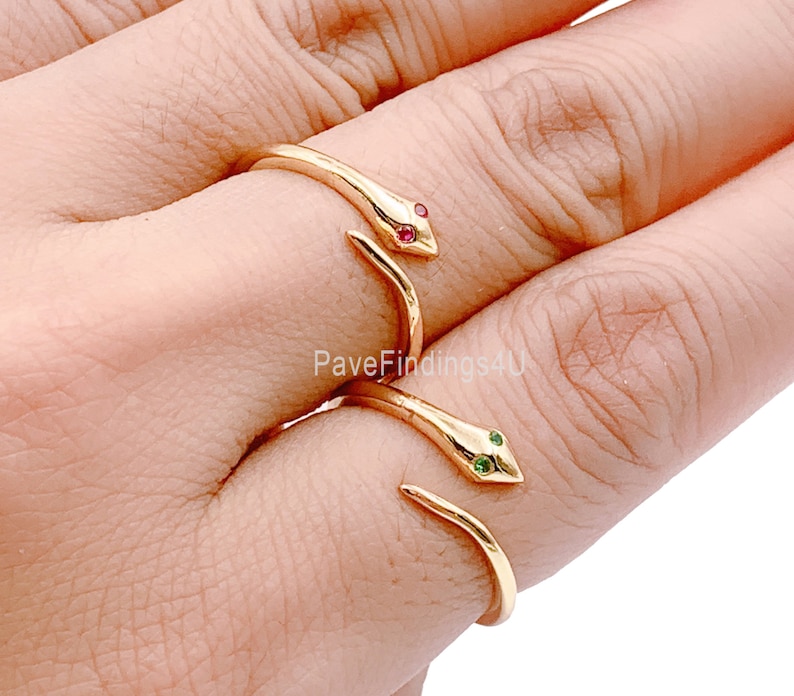 May include: Two gold snake rings with red and green gemstones. The rings are worn on the index and middle fingers of a hand.