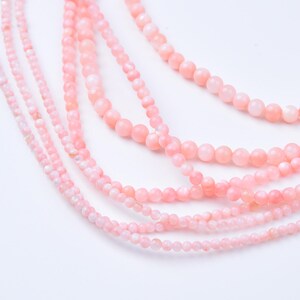May include: Close-up of several strands of pink gemstone beads. The beads vary in size, with some strands featuring smaller, more delicate beads and others with larger, more prominent ones. The color is a soft, pastel pink, creating a gentle and feminine aesthetic.