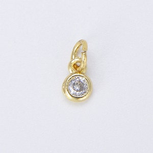 Puede incluir: Un charm dorado con un pequeño strass transparente en el centro. El charm tiene un bucle en la parte superior para sujetarlo a un collar o pulsera.