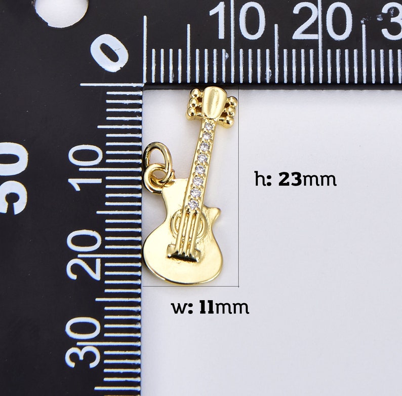 May include: Gold-tone guitar charm with clear rhinestones. The charm is 23 mm high and 11 mm wide.