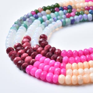 May include: Close-up of several strands of faceted gemstone beads in a variety of colors. The beads include shades of pink, red, white, green, and purple. The beads are strung together, creating a colorful and textured display.